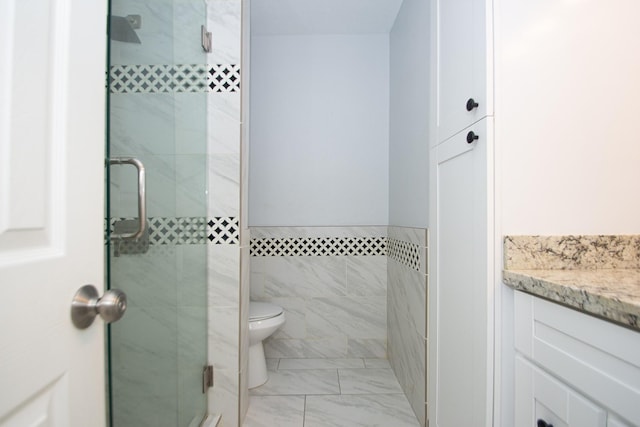 bathroom with vanity, a shower with shower door, tile walls, and toilet