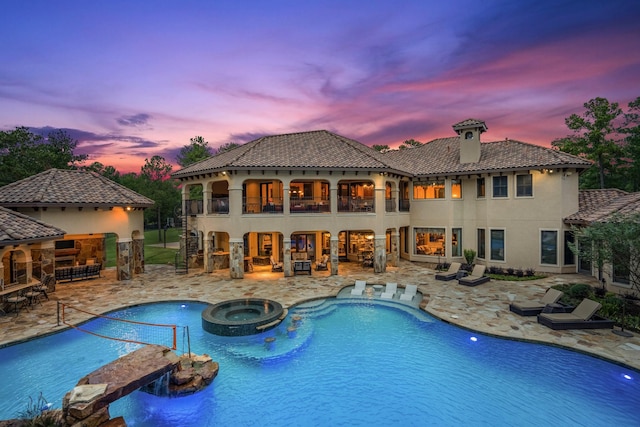 pool at dusk with an in ground hot tub and a patio