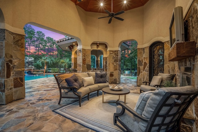 patio terrace at dusk with an outdoor living space with a fireplace and ceiling fan