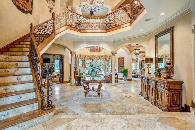 entrance foyer featuring an inviting chandelier, a towering ceiling, crown molding, and decorative columns