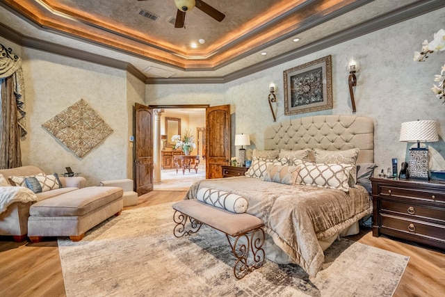 bedroom with decorative columns, light wood-type flooring, crown molding, and a tray ceiling