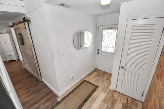 entryway featuring hardwood / wood-style flooring, crown molding, a barn door, and wood walls