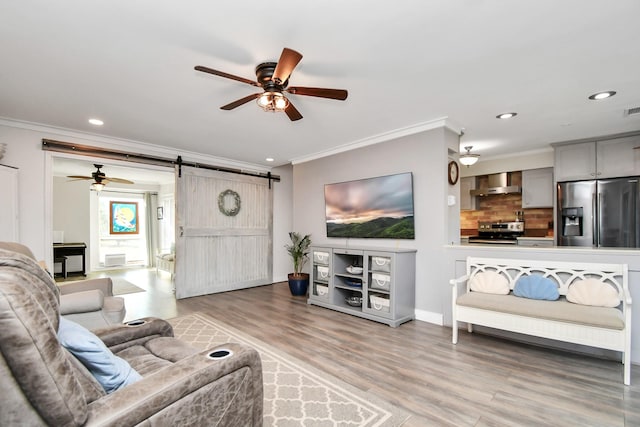 living room featuring crown molding, wood-type flooring, a barn door, and ceiling fan