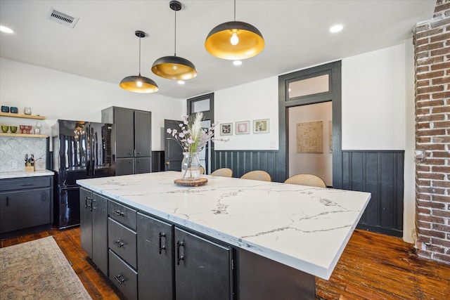 kitchen with black refrigerator, a kitchen breakfast bar, light stone countertops, pendant lighting, and a center island