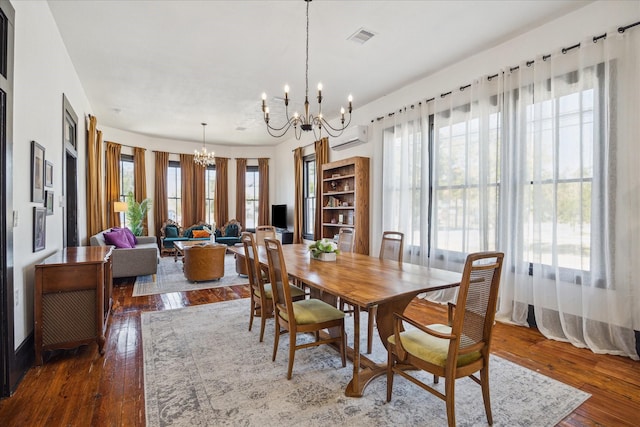 dining space featuring a wall unit AC, dark wood-type flooring, a healthy amount of sunlight, and an inviting chandelier