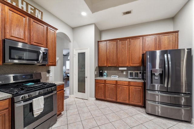 kitchen with light stone countertops, light tile patterned floors, backsplash, and appliances with stainless steel finishes