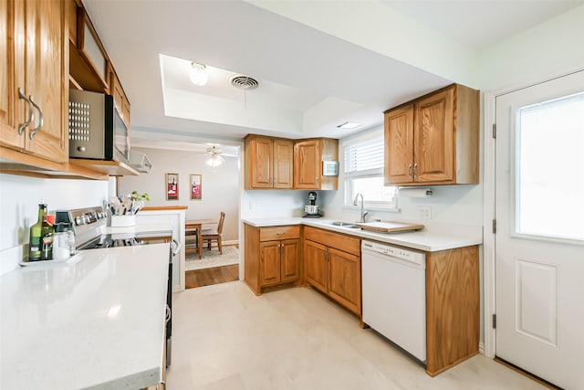 kitchen featuring dishwasher, stove, a raised ceiling, sink, and ceiling fan