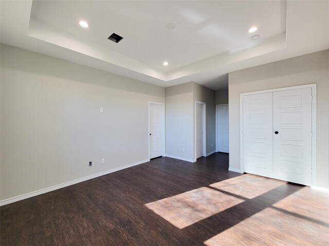 unfurnished bedroom featuring a raised ceiling and dark wood-type flooring