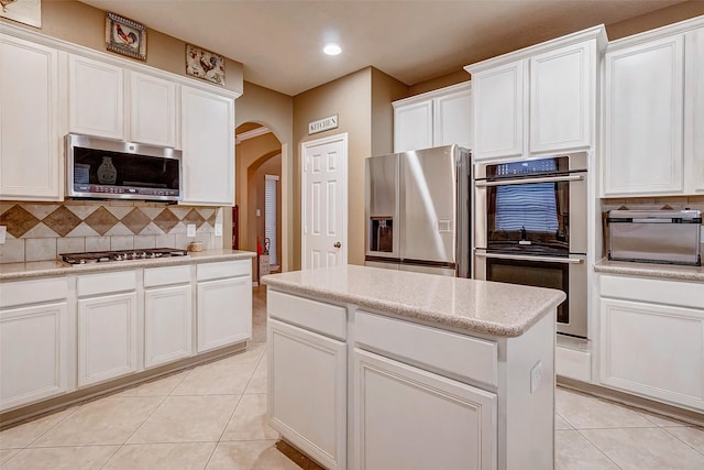 kitchen with backsplash, white cabinets, light stone countertops, appliances with stainless steel finishes, and light tile patterned flooring