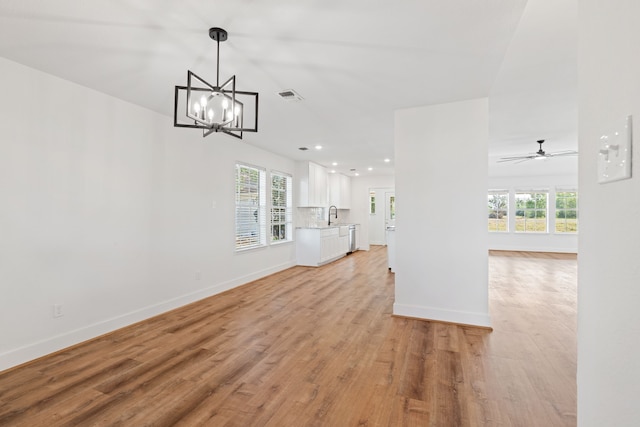 unfurnished living room with ceiling fan with notable chandelier, plenty of natural light, sink, and light hardwood / wood-style flooring