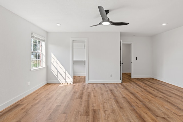 unfurnished bedroom featuring a spacious closet, a closet, ceiling fan, and light wood-type flooring