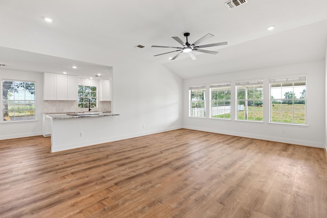 unfurnished living room featuring a wealth of natural light, ceiling fan, lofted ceiling, and light wood-type flooring