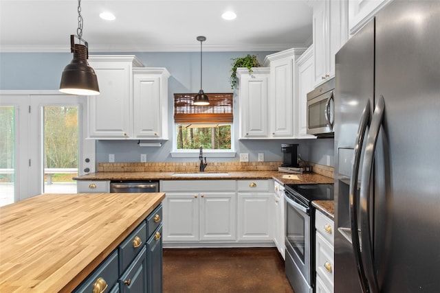 kitchen with appliances with stainless steel finishes, hanging light fixtures, white cabinets, sink, and butcher block counters