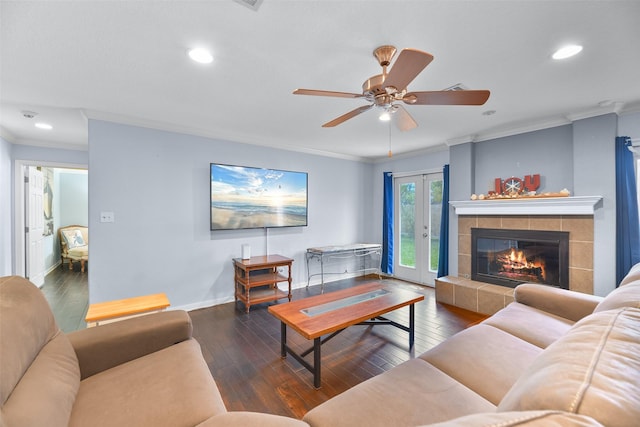 living room with a tile fireplace, dark wood-type flooring, ceiling fan, and crown molding