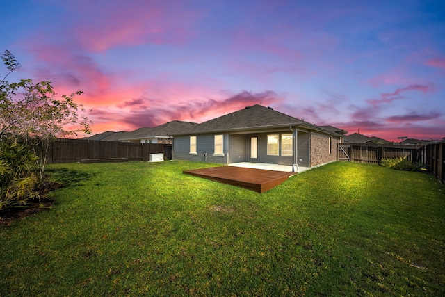 back house at dusk with a lawn and a deck