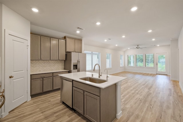 kitchen with backsplash, a center island with sink, sink, ceiling fan, and stainless steel appliances