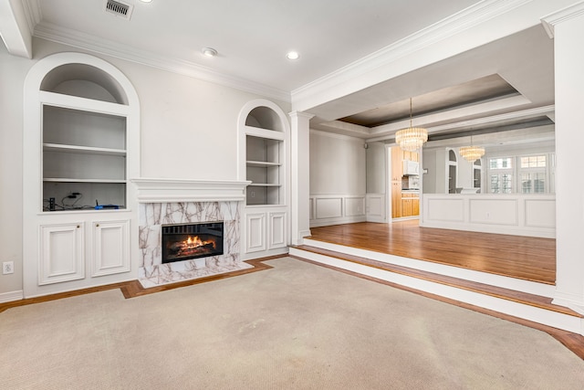 unfurnished living room with a raised ceiling, crown molding, an inviting chandelier, built in features, and a fireplace