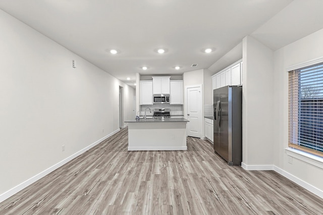 kitchen with backsplash, a kitchen island with sink, appliances with stainless steel finishes, light hardwood / wood-style floors, and white cabinetry