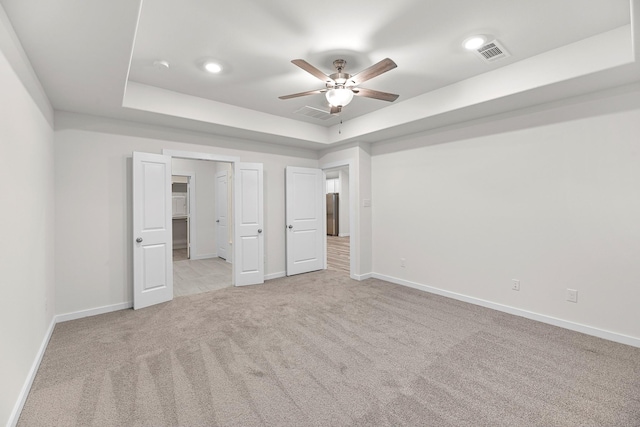 unfurnished bedroom featuring ceiling fan, a raised ceiling, and light colored carpet