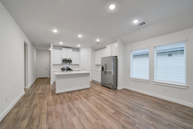 kitchen with a center island with sink, light hardwood / wood-style floors, white cabinets, and appliances with stainless steel finishes