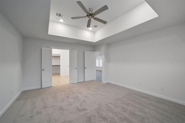 unfurnished bedroom featuring ceiling fan, a tray ceiling, light carpet, and a spacious closet