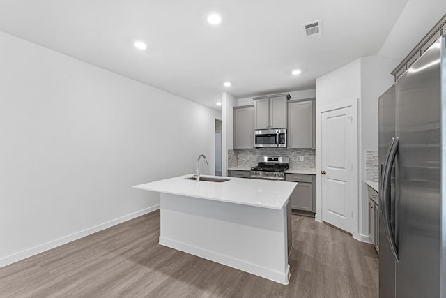 kitchen featuring tasteful backsplash, stainless steel appliances, a kitchen island with sink, sink, and gray cabinets