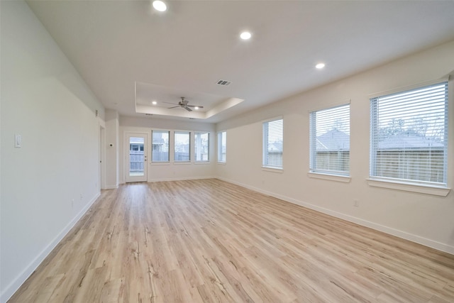 unfurnished room with ceiling fan, a tray ceiling, light hardwood / wood-style floors, and a healthy amount of sunlight