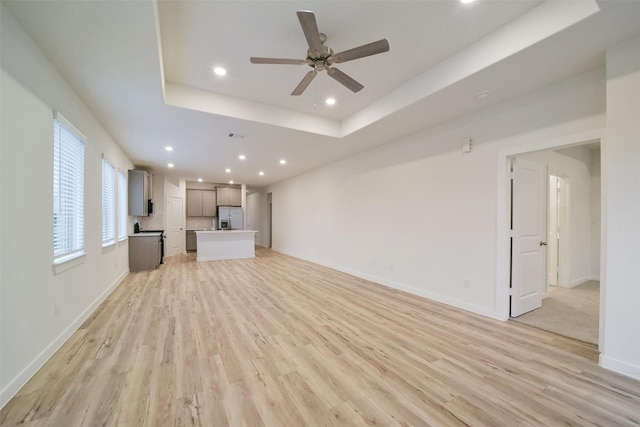 unfurnished living room with ceiling fan, a raised ceiling, and light wood-type flooring