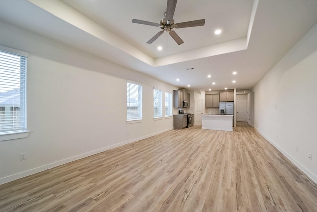 unfurnished living room with light hardwood / wood-style flooring, a raised ceiling, and ceiling fan