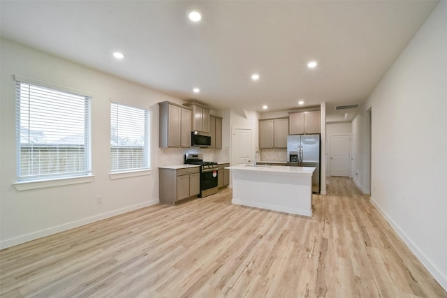 kitchen featuring an island with sink, sink, backsplash, stainless steel appliances, and light hardwood / wood-style flooring