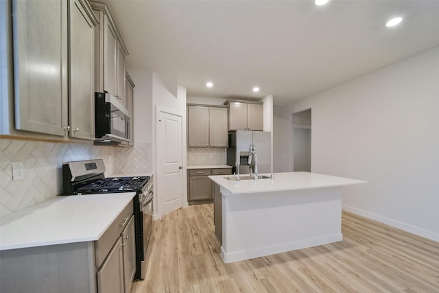 kitchen featuring stainless steel appliances, sink, a center island with sink, and light hardwood / wood-style flooring