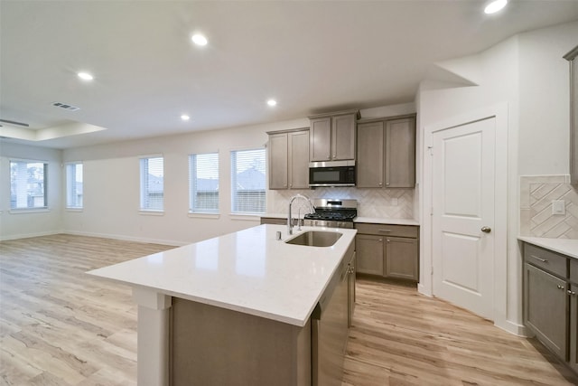 kitchen with sink, tasteful backsplash, light hardwood / wood-style flooring, appliances with stainless steel finishes, and a kitchen island with sink