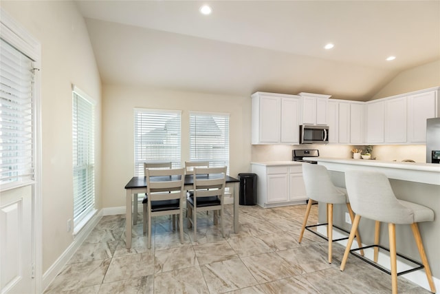 kitchen featuring a breakfast bar, stainless steel appliances, white cabinetry, and lofted ceiling