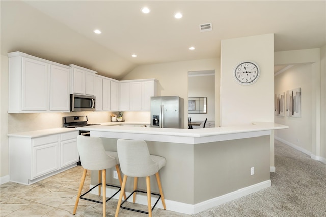 kitchen featuring white cabinetry, a kitchen breakfast bar, vaulted ceiling, light carpet, and appliances with stainless steel finishes