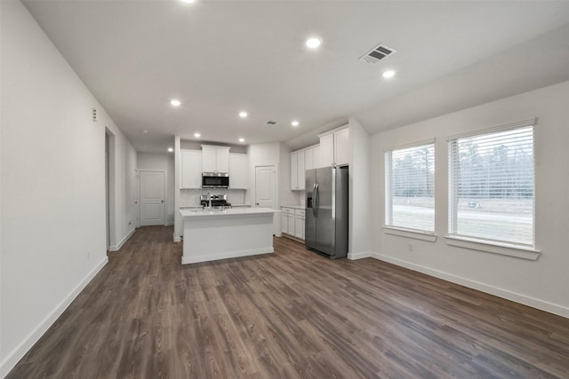 kitchen featuring stainless steel appliances, an island with sink, white cabinets, dark hardwood / wood-style flooring, and decorative backsplash