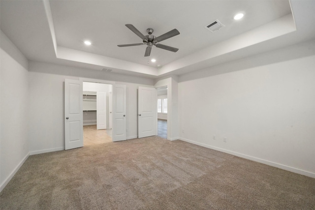 unfurnished bedroom featuring a spacious closet, light colored carpet, ceiling fan, and a tray ceiling