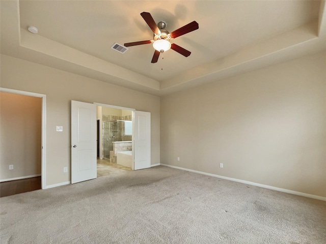 unfurnished bedroom with ensuite bath, ceiling fan, light carpet, and a tray ceiling