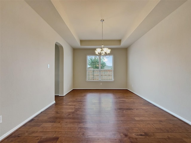 unfurnished room featuring a notable chandelier, a raised ceiling, and dark wood-type flooring