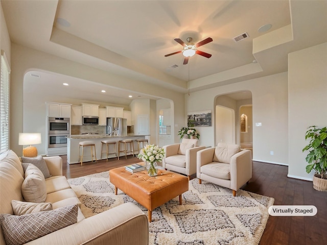 living room with ceiling fan, dark hardwood / wood-style flooring, and a raised ceiling