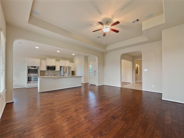 unfurnished living room featuring ceiling fan, dark hardwood / wood-style floors, and a tray ceiling