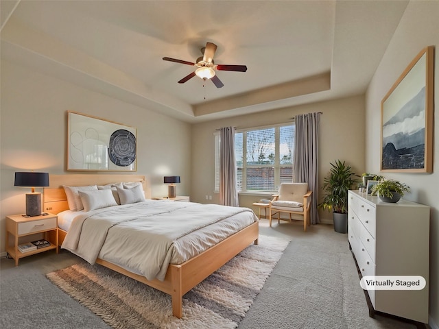 bedroom with a raised ceiling, ceiling fan, and carpet flooring