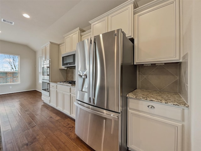 kitchen with backsplash, light stone counters, stainless steel appliances, dark wood-type flooring, and lofted ceiling