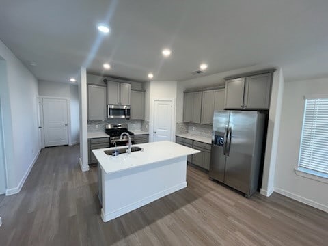 kitchen featuring sink, decorative backsplash, an island with sink, appliances with stainless steel finishes, and dark hardwood / wood-style flooring