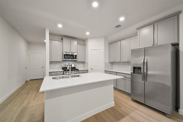 kitchen featuring appliances with stainless steel finishes, gray cabinets, a center island with sink, and light hardwood / wood-style flooring