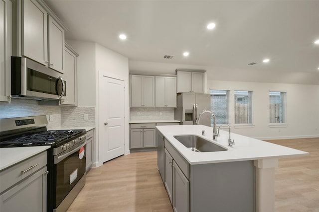 kitchen with an island with sink, appliances with stainless steel finishes, gray cabinets, and sink