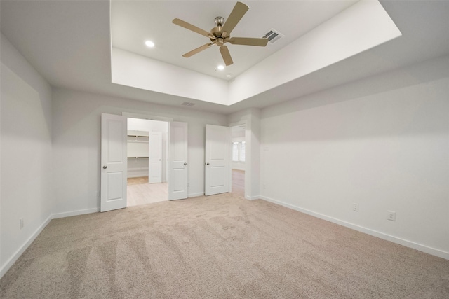 unfurnished bedroom featuring a spacious closet, light carpet, ceiling fan, and a tray ceiling