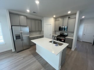 kitchen featuring gray cabinetry, decorative backsplash, stainless steel appliances, and wood-type flooring