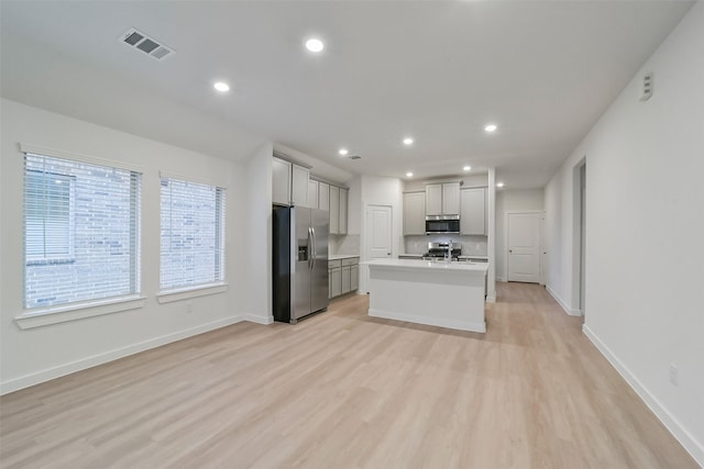 kitchen featuring light hardwood / wood-style flooring, gray cabinets, stainless steel appliances, tasteful backsplash, and a center island with sink