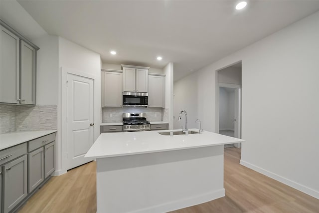 kitchen featuring sink, light hardwood / wood-style flooring, gray cabinets, an island with sink, and stainless steel range with gas cooktop