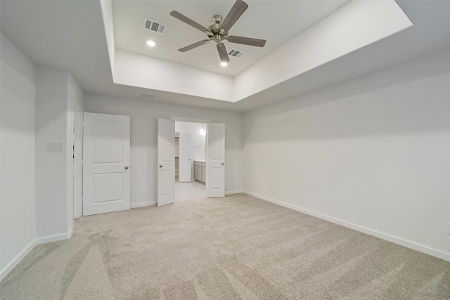 unfurnished bedroom featuring ceiling fan, connected bathroom, a raised ceiling, and light carpet